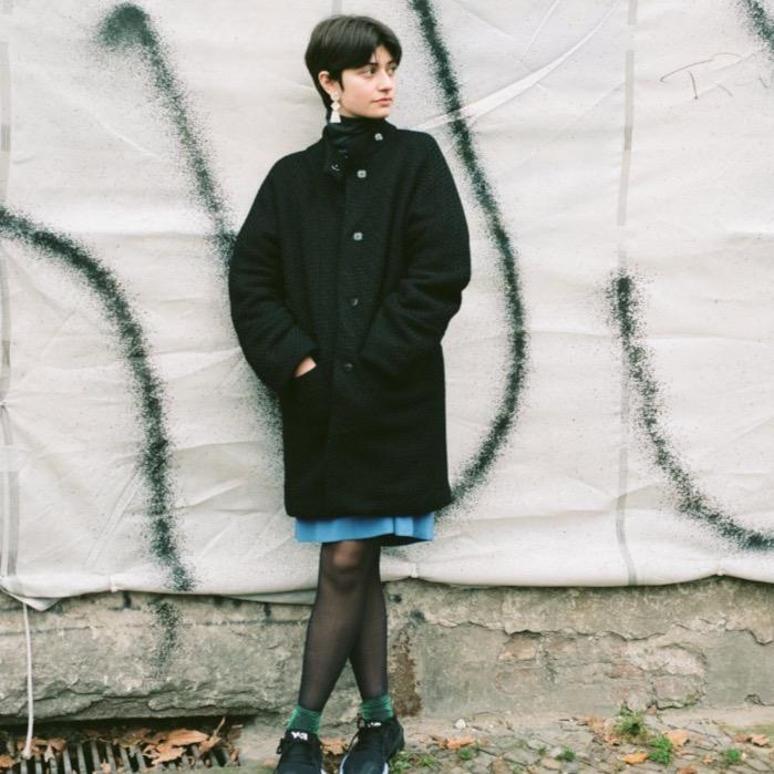 black canvas-weave sparkling effect coat with kimono sleeves, cashmere wool, snap closures. The jacket keeps warm as merino wool traps the heat. The model is wearing apres ski earrings and Y3 sneakers. cruba