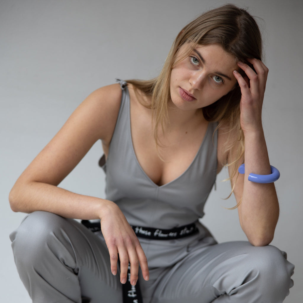 Our model is wearing our grey overall made out of cotton. The model is wearing a size L to get an oversized fit and with a canvas belt around her waist to hug her figure. She is also wearing the wooden bangle covered in a lilac colour from uncommon matters. cruba