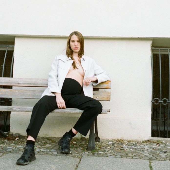 Pregnancy pants with a loose fit. The black work maternity pants are flattering for and lend support and comfort. The model is wearing the maternity pants with sneakers and a white cargo jacket. cruba